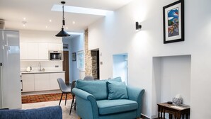 A modern living room with a teal sofa, a dining area with a small table and chairs, and a kitchen in the background.