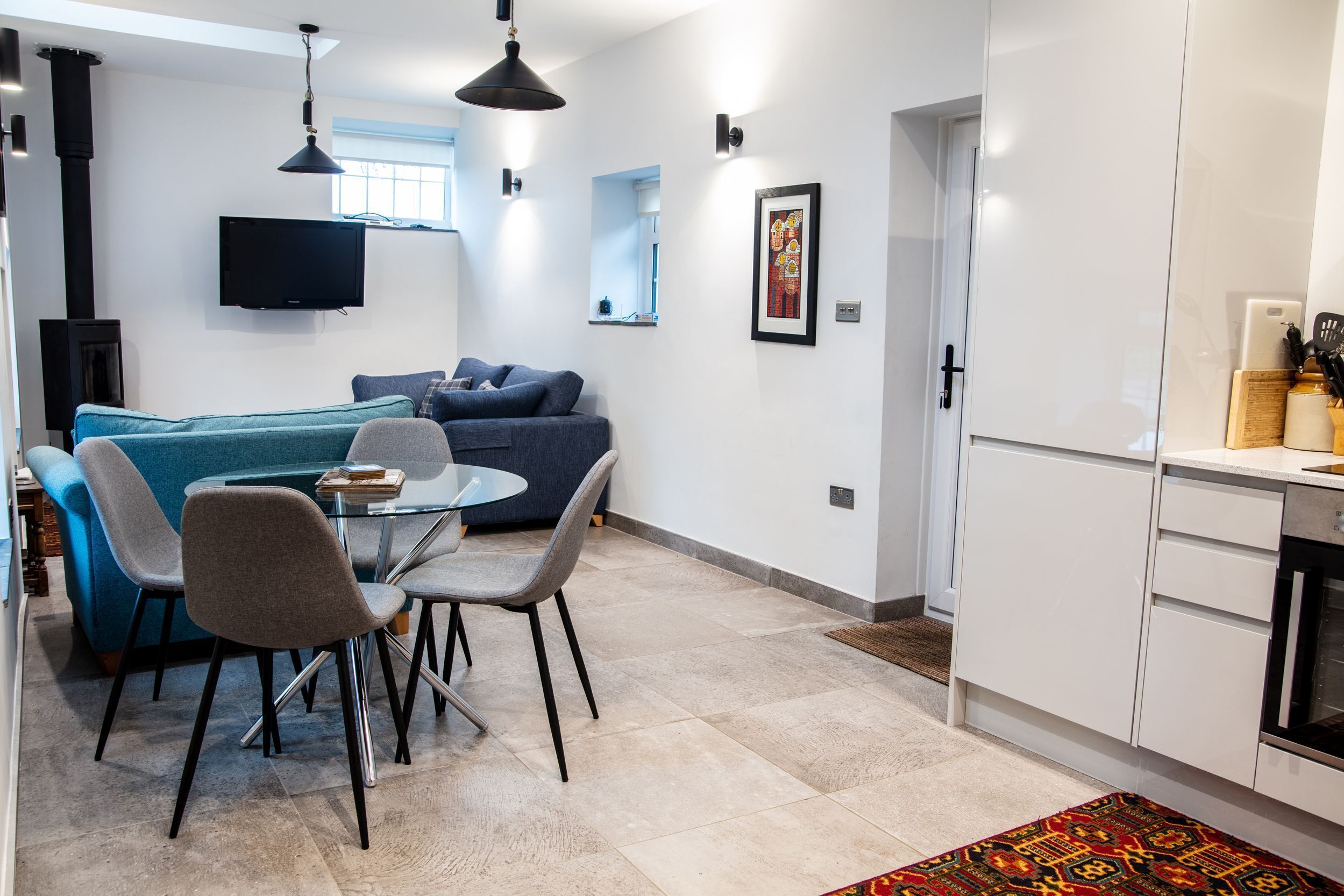 A modern living room with a sofa, chairs, a dining table, a TV, and a kitchen area with cabinets and appliances.