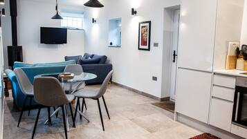 A modern living room with a sofa, chairs, a dining table, a TV, and a kitchen area with cabinets and appliances.