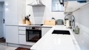 A modern kitchen with white cabinetry, a stainless steel range hood, a built-in oven, a sink with a faucet, and a window above the sink.