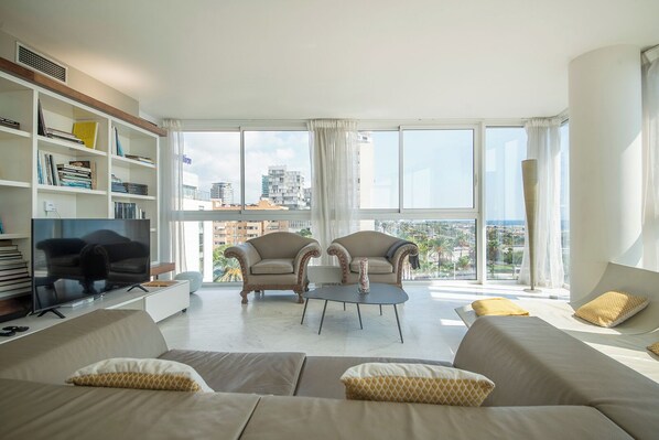 Una sala de estar moderna con una gran televisión de pantalla plana, dos sillones, un sofá y una estantería.