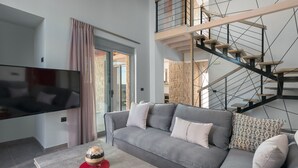 A modern living room with a grey sofa, a flat-screen TV, and a staircase with a wooden finish.