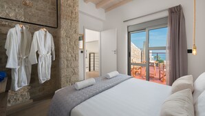 A bedroom with a large bed, a stone wall, and a balcony with a view.