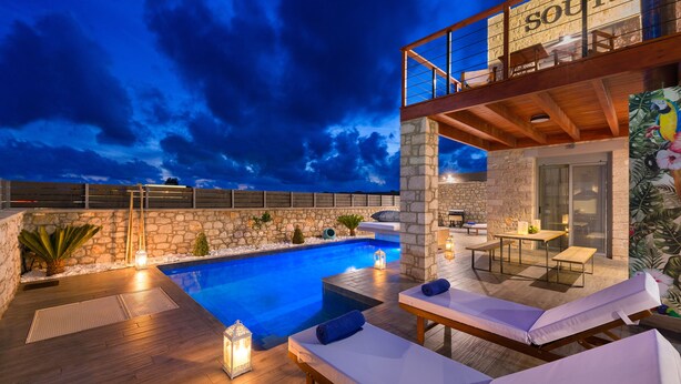 A rooftop pool area with lounge chairs, a stone wall, and a wooden deck.