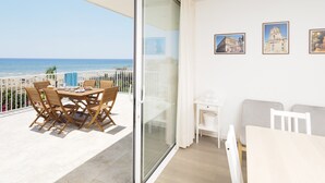 A balcony with a table and chairs, a sofa, a small table with a lamp, and a glass door leading to a beach view.