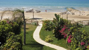 A pathway leading to a beach with a thatched umbrella and a view of the ocean.