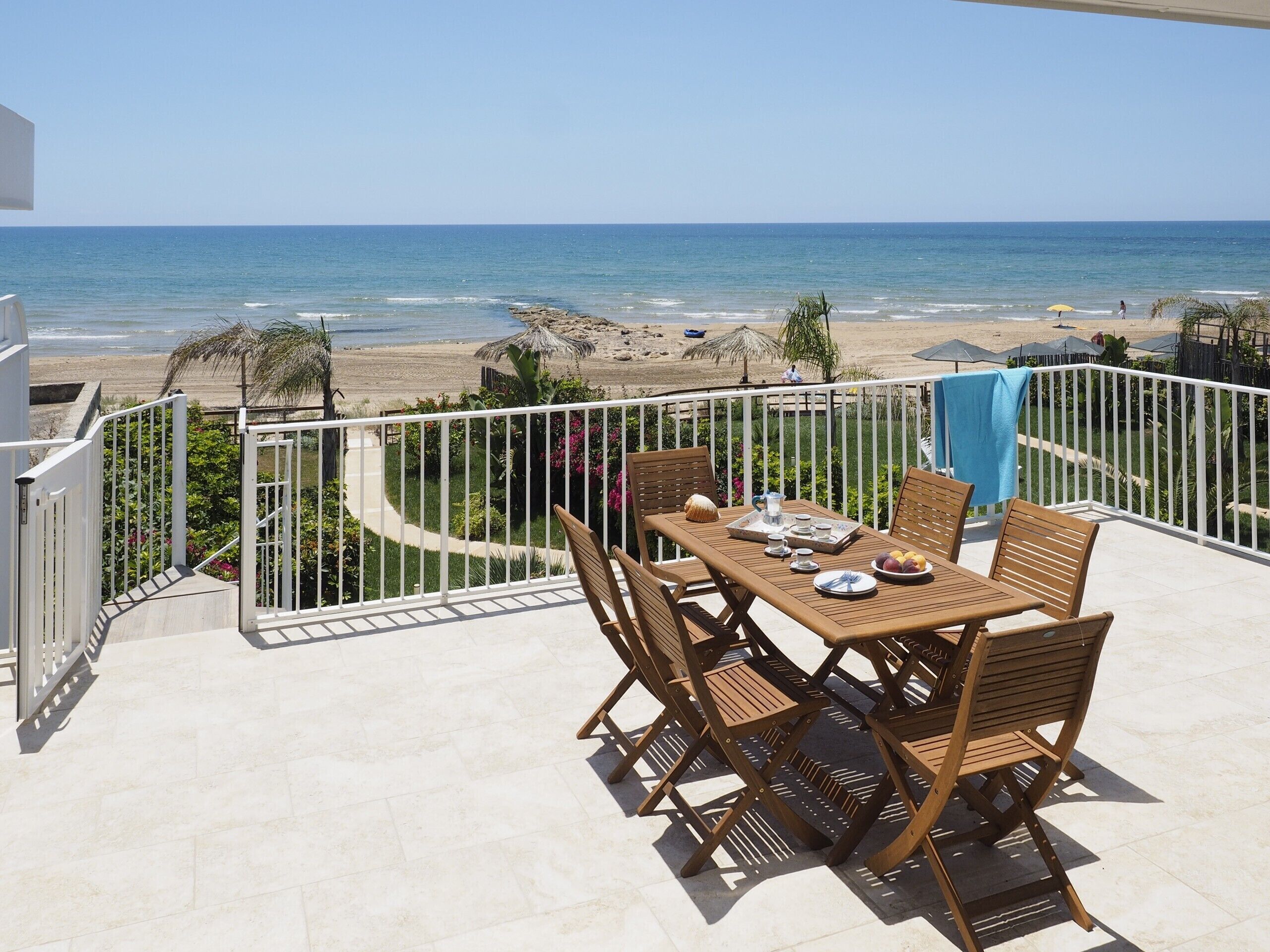 A balcony with a table and chairs overlooking a beach.