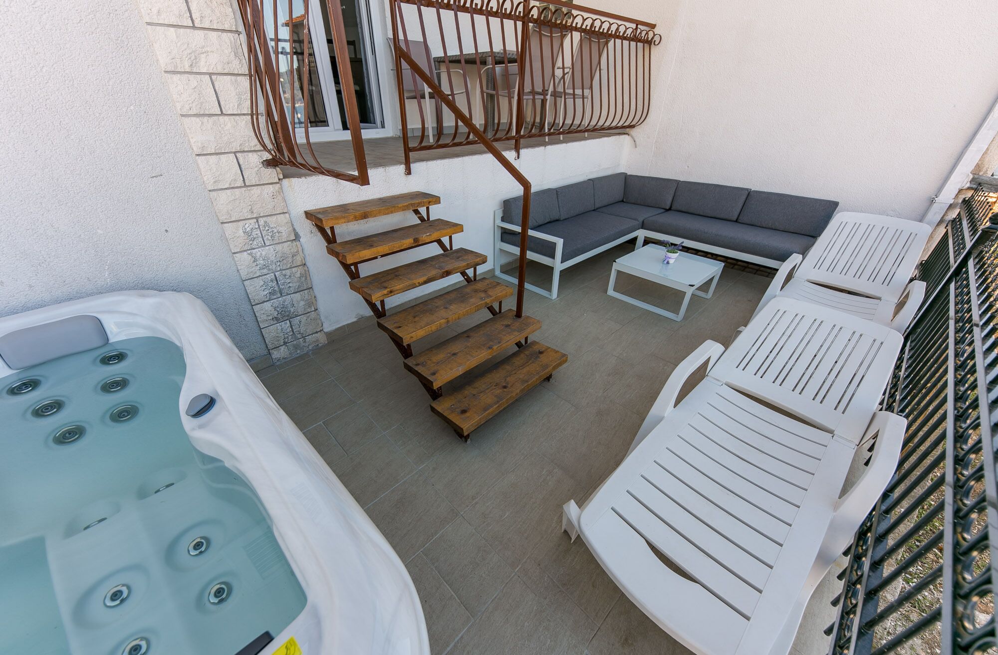 Un'area patio con vasca idromassaggio, scalini in legno, divano, tavolino da caffè e poltrone relax.