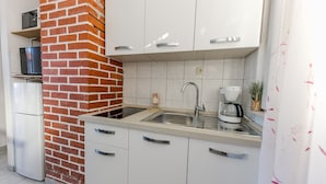 A compact kitchen with white cabinets, a brick accent wall, a stainless steel sink, and a coffee maker. - Seafront app with jacuzzi and huge terrace (Vinišće)