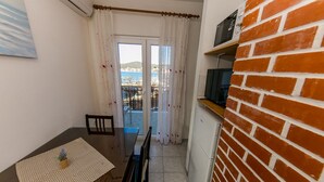 A small, narrow room with a dining table and chairs, a television on a brick wall, and a view of the sea through a door. - Seafront app with jacuzzi and huge terrace (Vinišće)