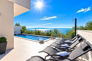 A pool area with lounge chairs and a view of the sea.