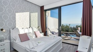 Une chambre moderne avec un grand lit, une vue sur la mer et un espace piscine visible à travers la porte vitrée.