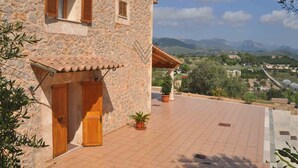 A stone building with wooden shutters, a tiled patio, and a view of a valley with mountains in the background. - Finca Can Mirlo in en Santa Maria (Marratxi)