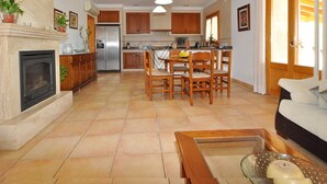 A spacious living room with a fireplace, a dining area, and a kitchen with wooden cabinets and a central island. - Finca Can Mirlo in en Santa Maria (Marratxi)
