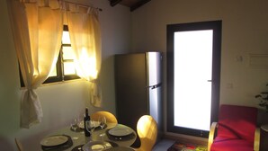 A dining area with a table set for two, a refrigerator, and a window with curtains.