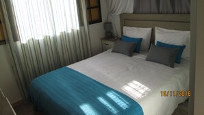 A bedroom with a bed, curtains, a nightstand, and a lamp.