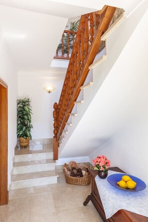 A staircase with wooden balusters, a potted plant, a wicker basket, and a table with a blue plate and yellow lemons.