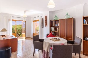 A room with a dining table, chairs, a bookshelf, and a view through a glass door.