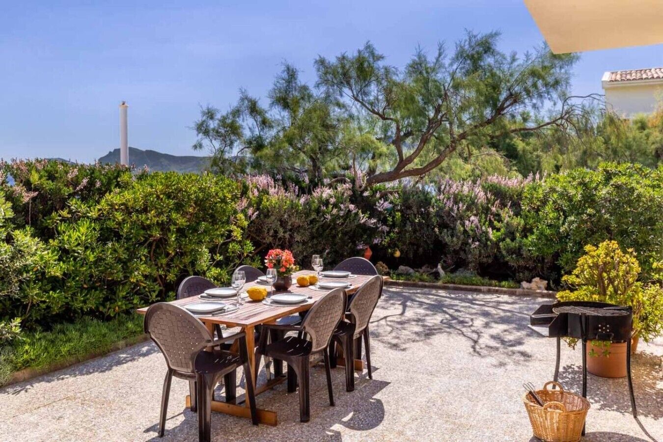 Un espacio para comer al aire libre con una mesa dispuesta para cuatro personas, rodeado de follaje y vistas del paisaje.