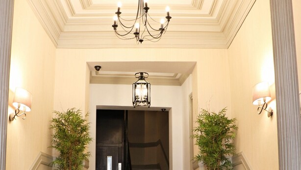 Una entrada imponente con escalones de mármol, un candelabro y dos plantas en macetas.