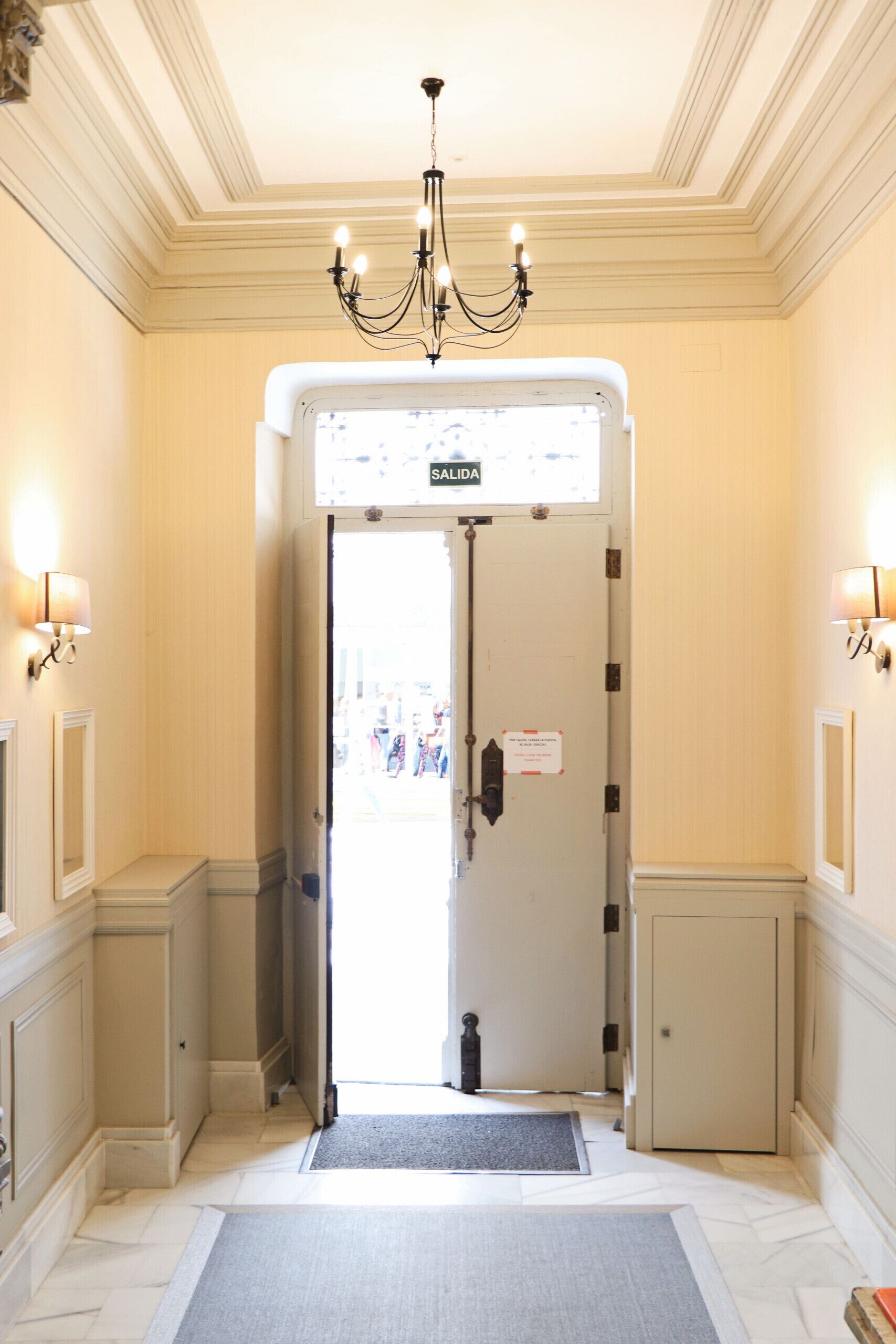 L’entrée d’un hôtel, avec un lustre, une enseigne indiquant « SORTIE » et un paillasson.