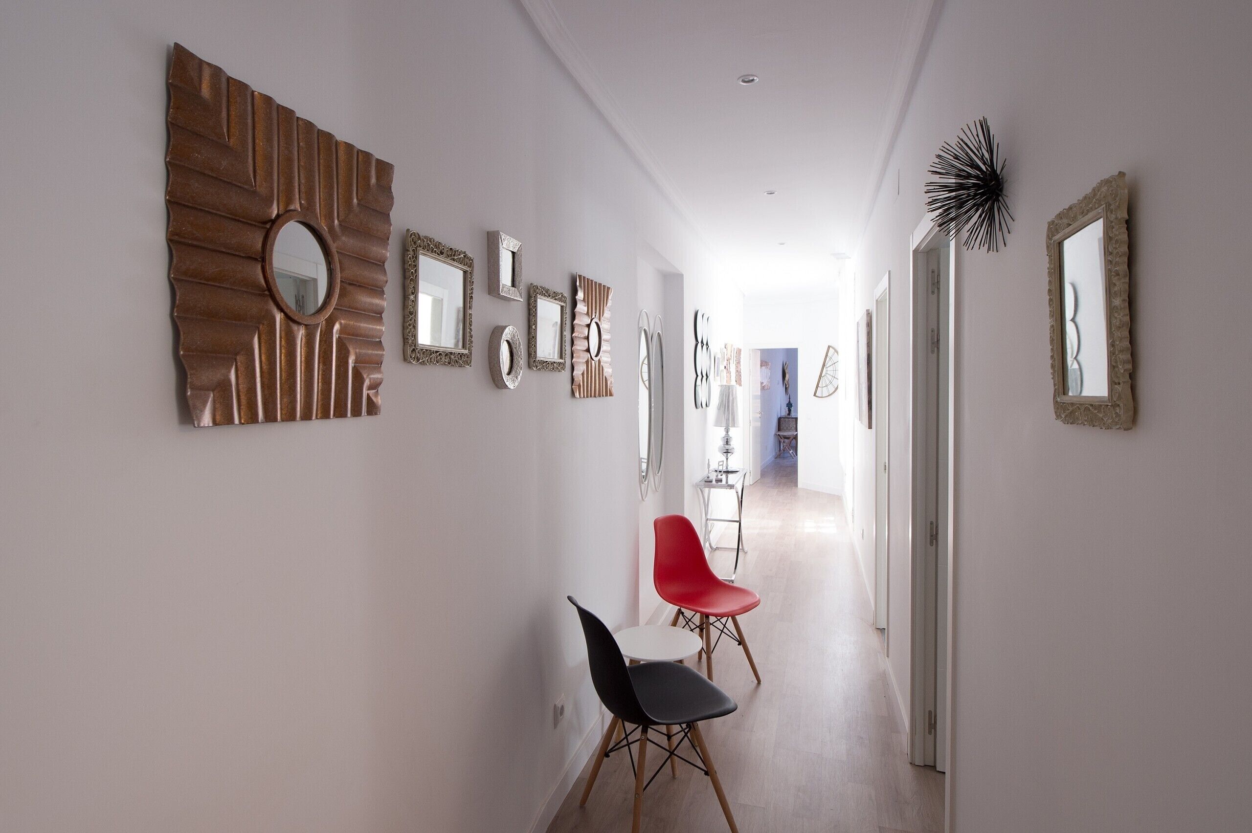 A hallway with various wall-mounted mirrors and a few chairs.