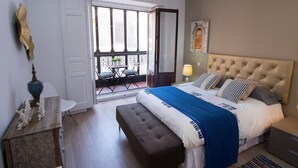 Un dormitorio con una cama grande, un banco, una mesa con una lámpara y vistas al balcón exterior.
