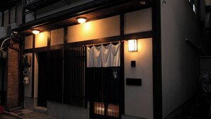 A traditional Japanese building with a black gate, white curtains, and two wall-mounted lights.