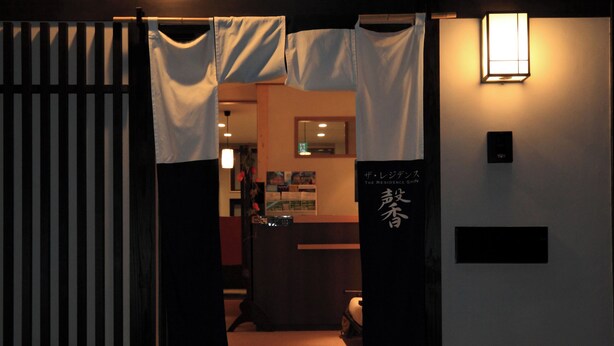 A traditional Japanese entrance with a wooden gate, a small reception desk, and a sign with Japanese characters.