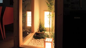 A room with a sliding glass door leading to a small outdoor area with a bamboo plant and a wooden bench.
