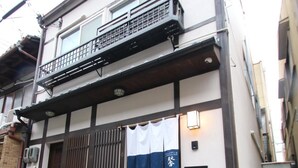 A two-story building with a balcony, a sliding door with a blue curtain, and a small step leading to the entrance.