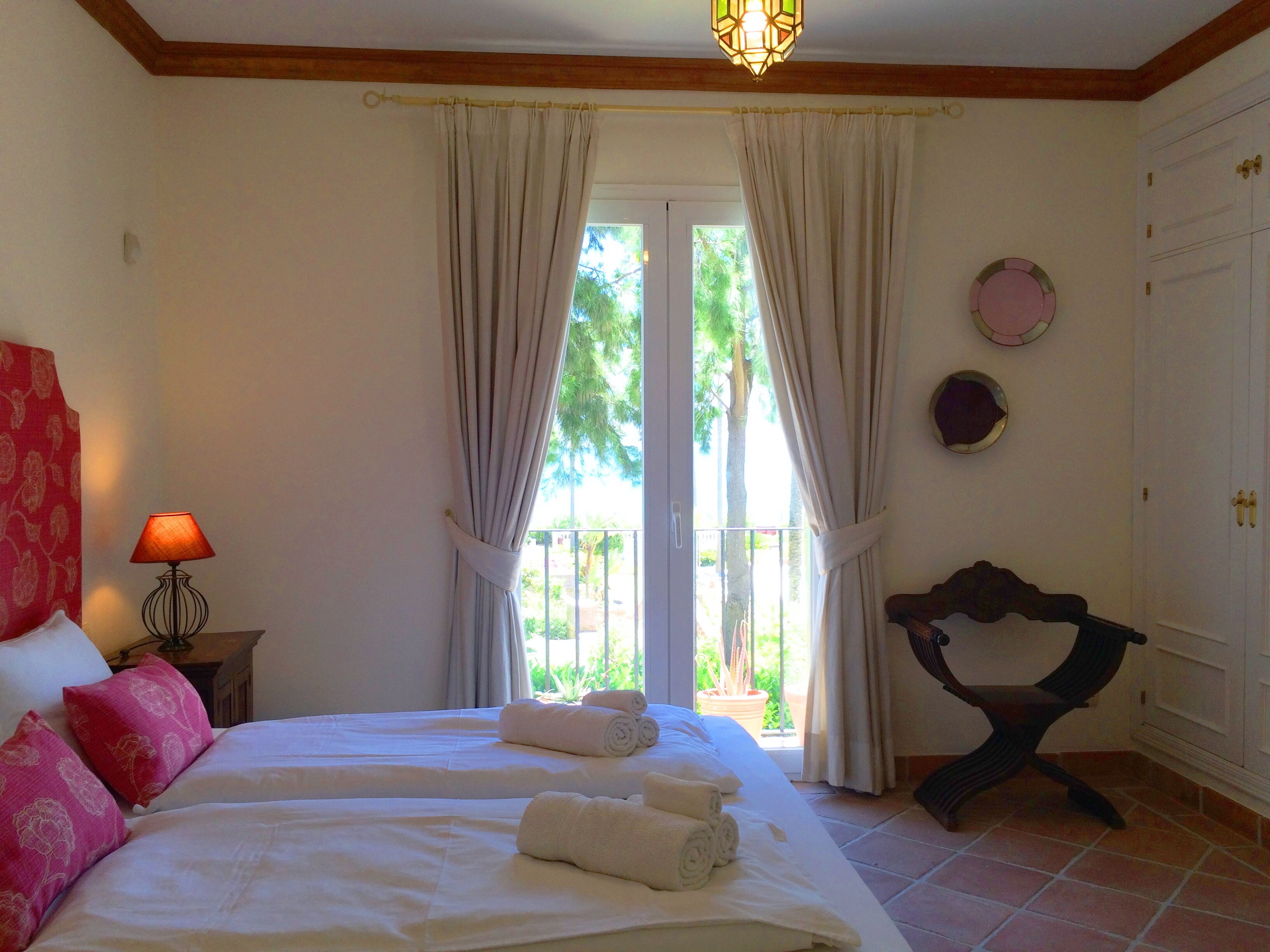 A hotel room with two beds, a balcony, a lamp, and a chair.