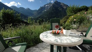Una mesa con un tazón de rebanadas de sandía, una jarra blanca y una planta en maceta, frente a un paisaje montañoso.
