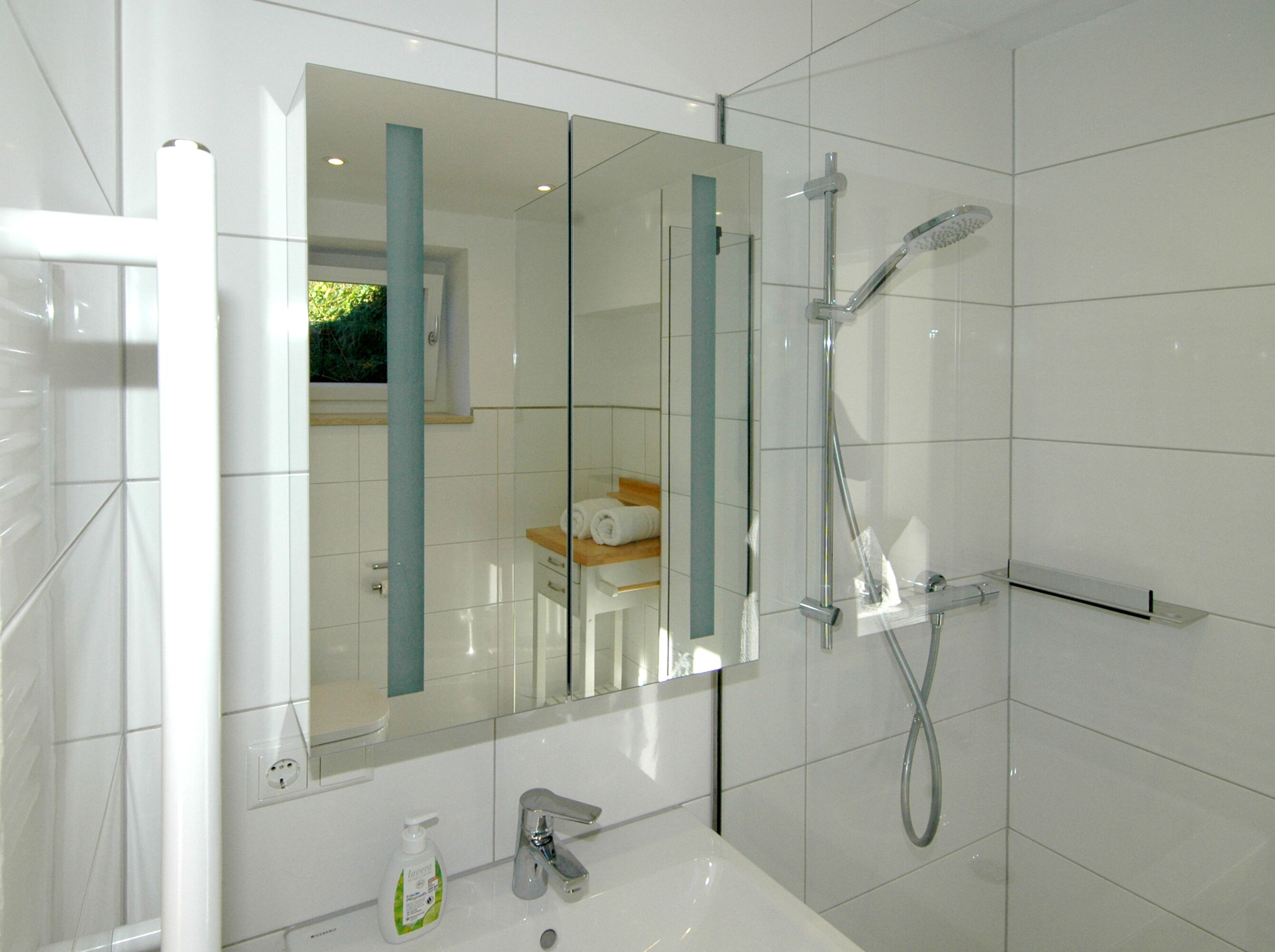 Une salle de bain moderne avec une douche à parois de verre, un lavabo blanc et un miroir agrémenté d’une touche de bleu.