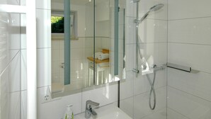 Un baño moderno con cabina de ducha de vidrio, un lavabo blanco y un espejo con detalles azules.