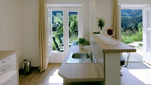 Una cocina moderna con un lavamanos integrado, una zona de comedor con mesa y sillas, y ventanas amplias que ofrecen vistas a un paisaje montañoso.