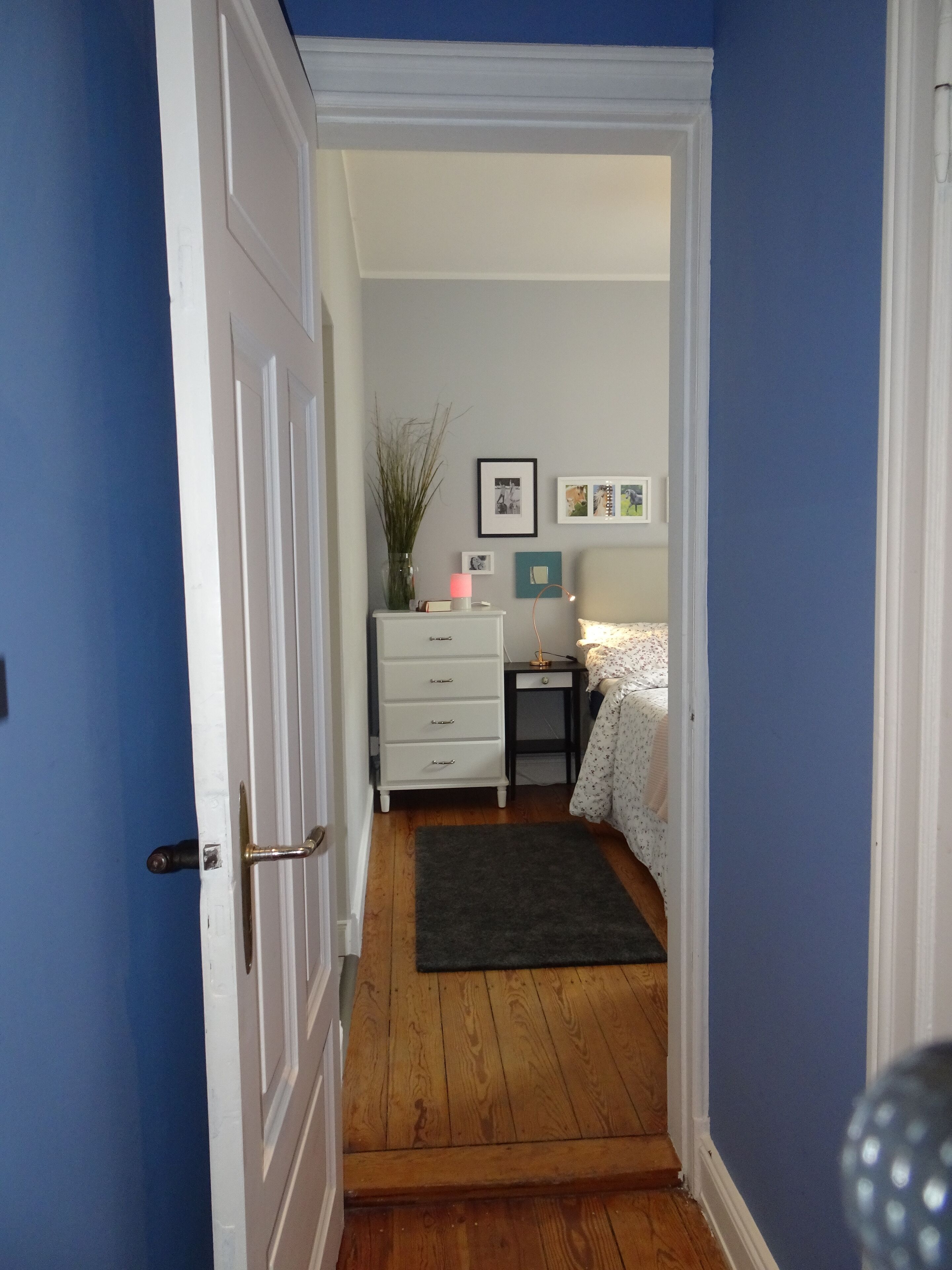 Una habitación con una puerta blanca, un lavabo y una pared de madera. Hay cuadros enmarcados en la pared y un armario pequeño.