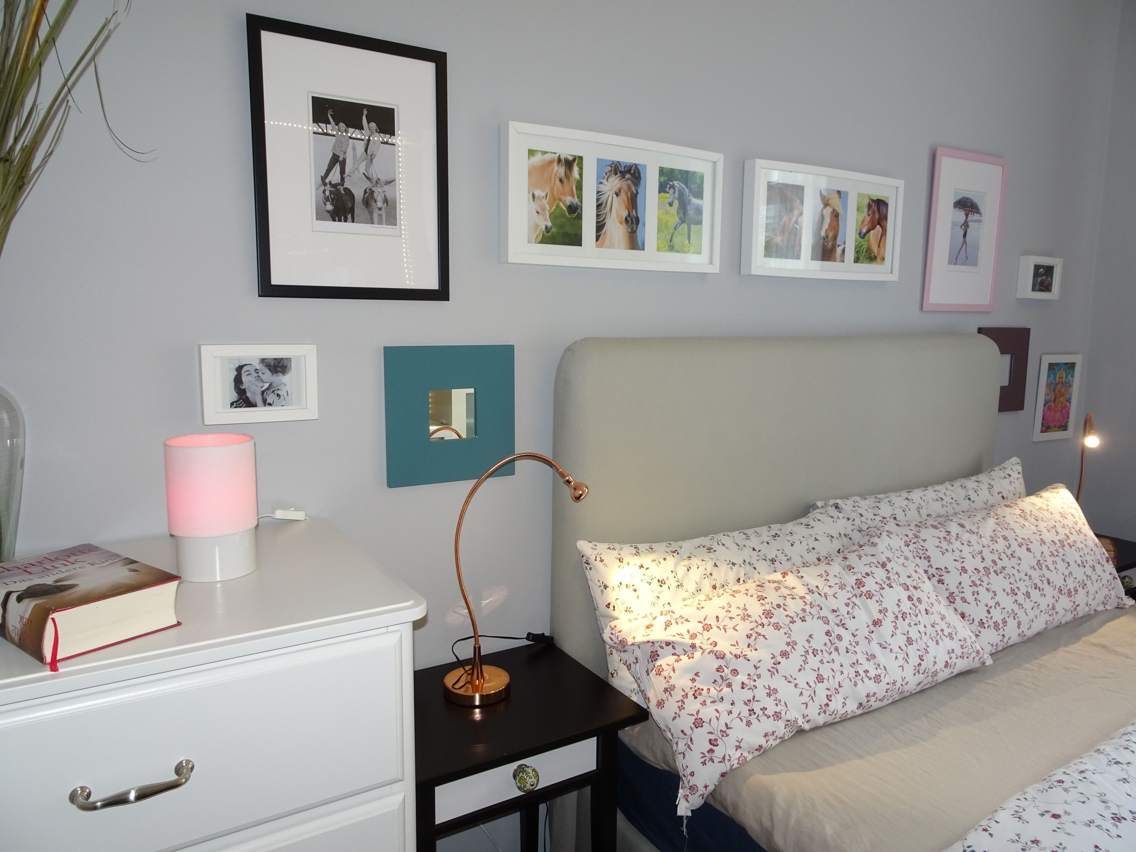Une chambre à coucher avec un lit, une table de chevet, une lampe et des tableaux accrochés au mur.