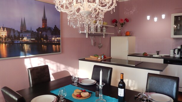 A dining area with a chandelier, a cityscape view, a kitchen, and a table set for a meal.