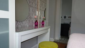 A bedroom with a bed, a vanity with a mirror, and a yellow ottoman.