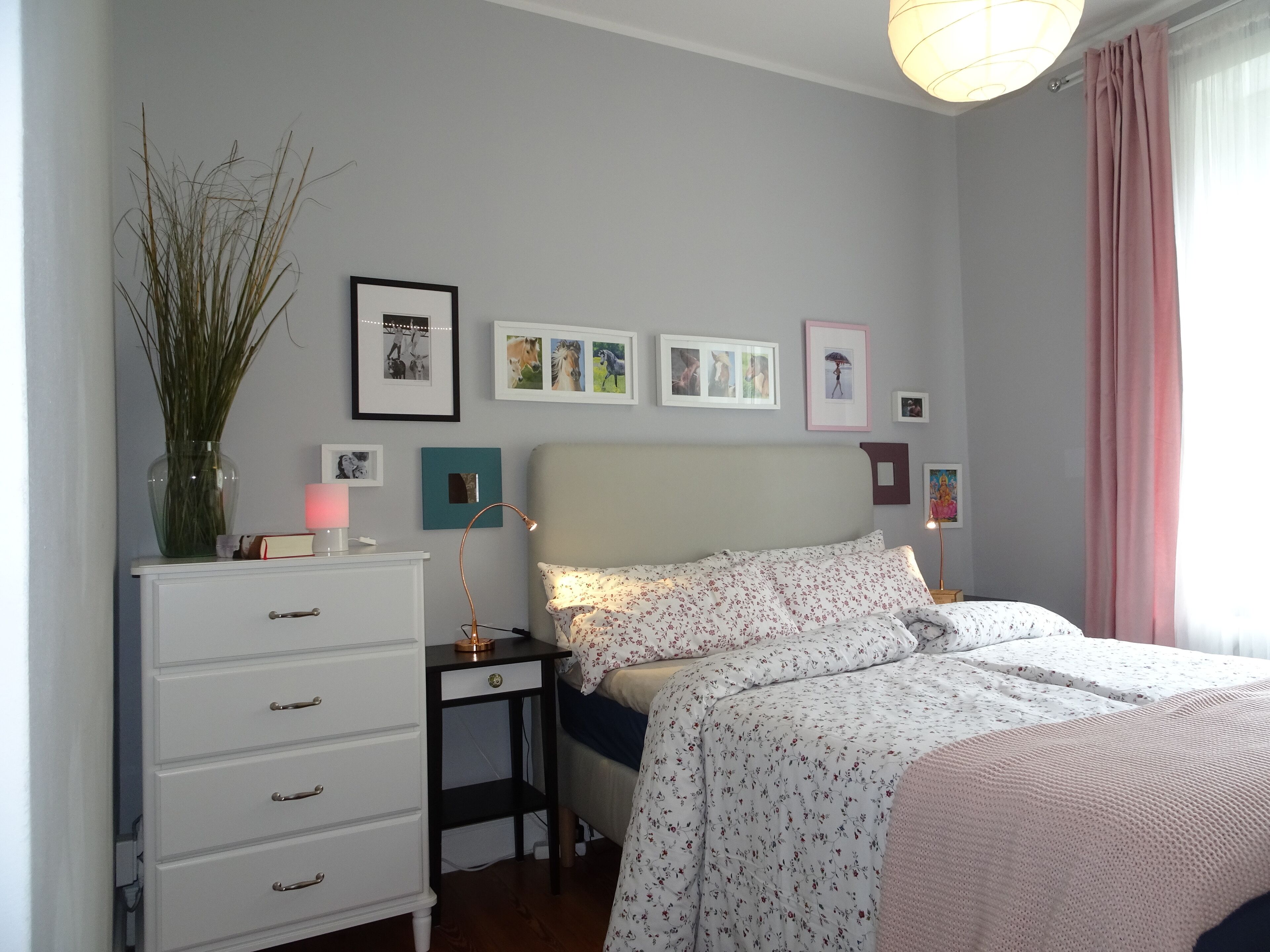 Un dormitorio con cama, mesita de noche, cómoda y cuadros colgados en la pared.