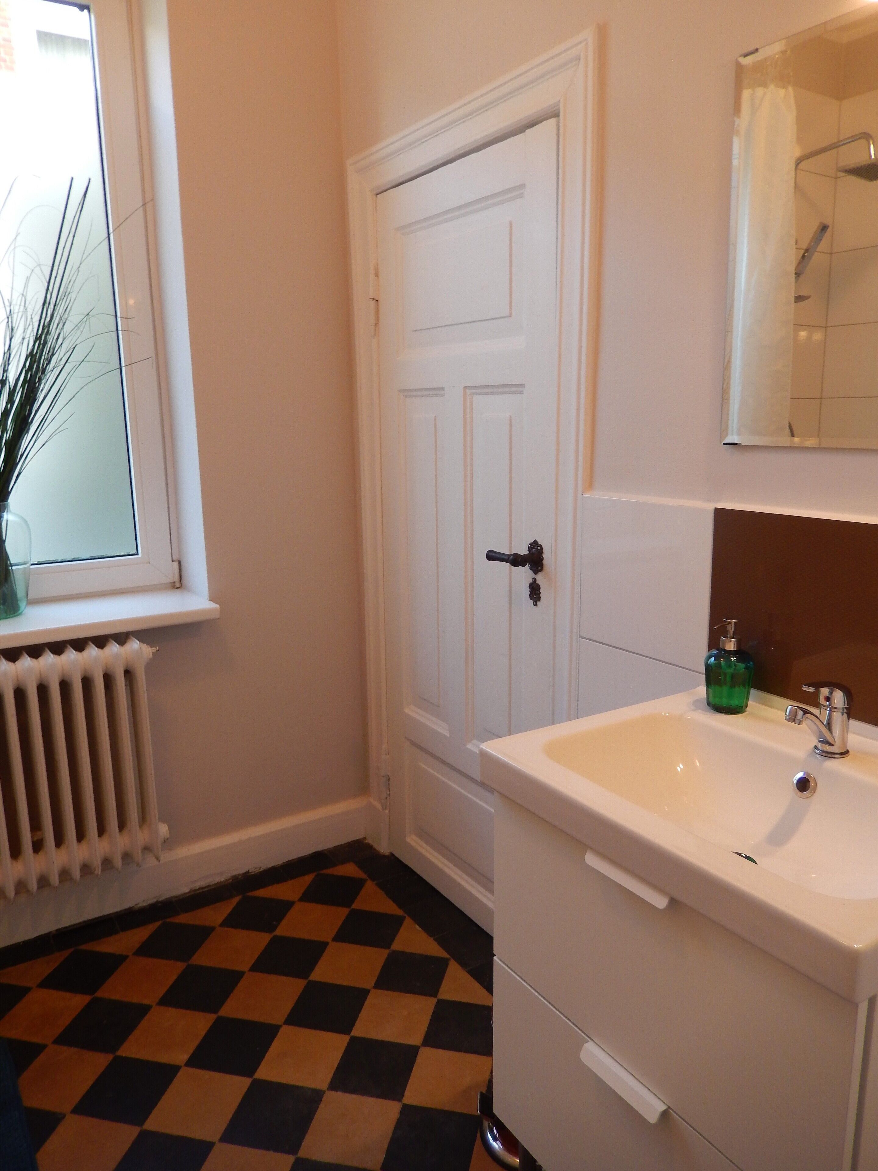 Ein Badezimmer mit Waschbecken, Spiegel, Tür und Heizkörper.