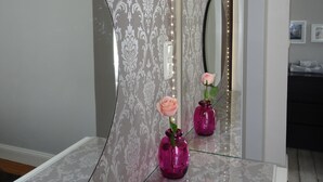 A bathroom with a large mirror, patterned wallpaper, and two pink vases with roses.