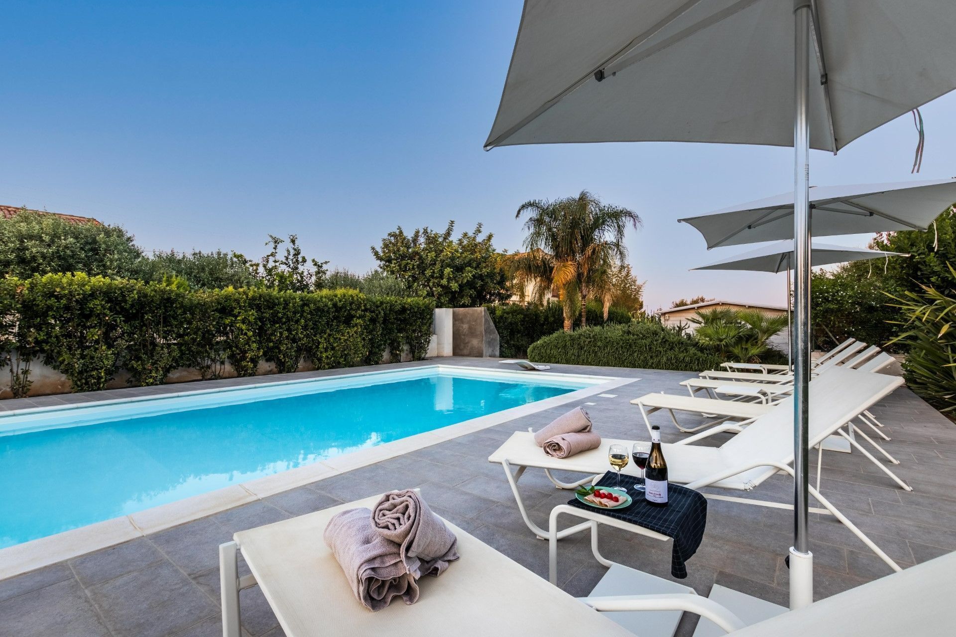 Un espace aménagé au bord de la piscine, avec des chaises longues, une table sur laquelle est posée une bouteille de vin et une serviette.