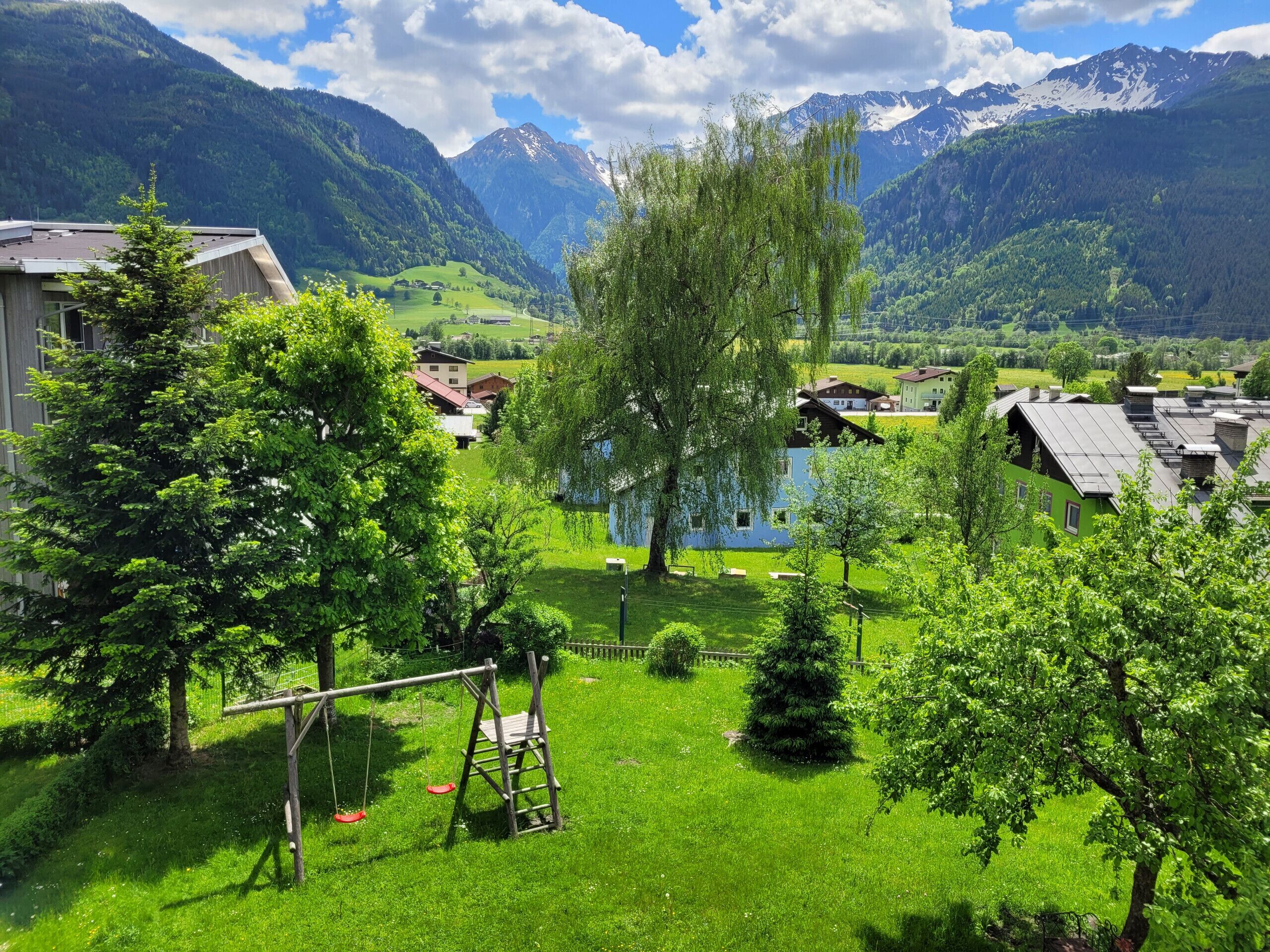 Ein Wohngebiet mit Häusern, einem Spielplatz und einer Bergkulisse im Hintergrund.