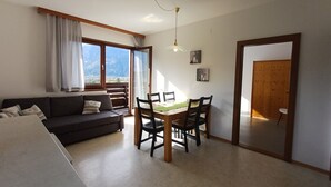 En moderne stue med sofa, spisebord og stole. Der er et stort vindue med gardiner, en loftlampe og kunst på væggene.