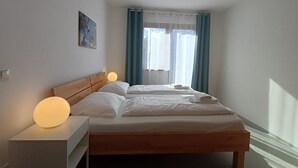 Et hotelværelse med to enkeltsenge, et natbord med lampe, et billede på væggen og et vindue med gardiner.