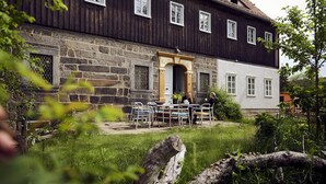 A two-story building with a stone facade and a wooden upper section. There is a small outdoor seating area with tables and chairs. - Large, lovingly renovated half-timbered house with sauna & garden (Ebersbach-Neugersdorf)