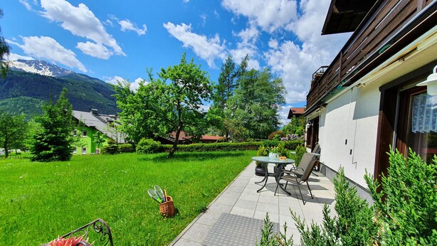 Une terrasse avec une table et des chaises, un petit jardin et une vue sur la montagne.