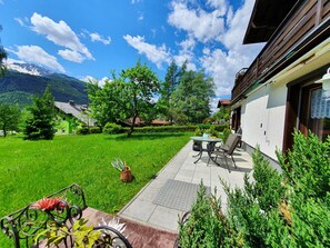 Eine Terrasse mit Tisch und Stühlen, ein kleiner Garten und Blick auf die Berge.
